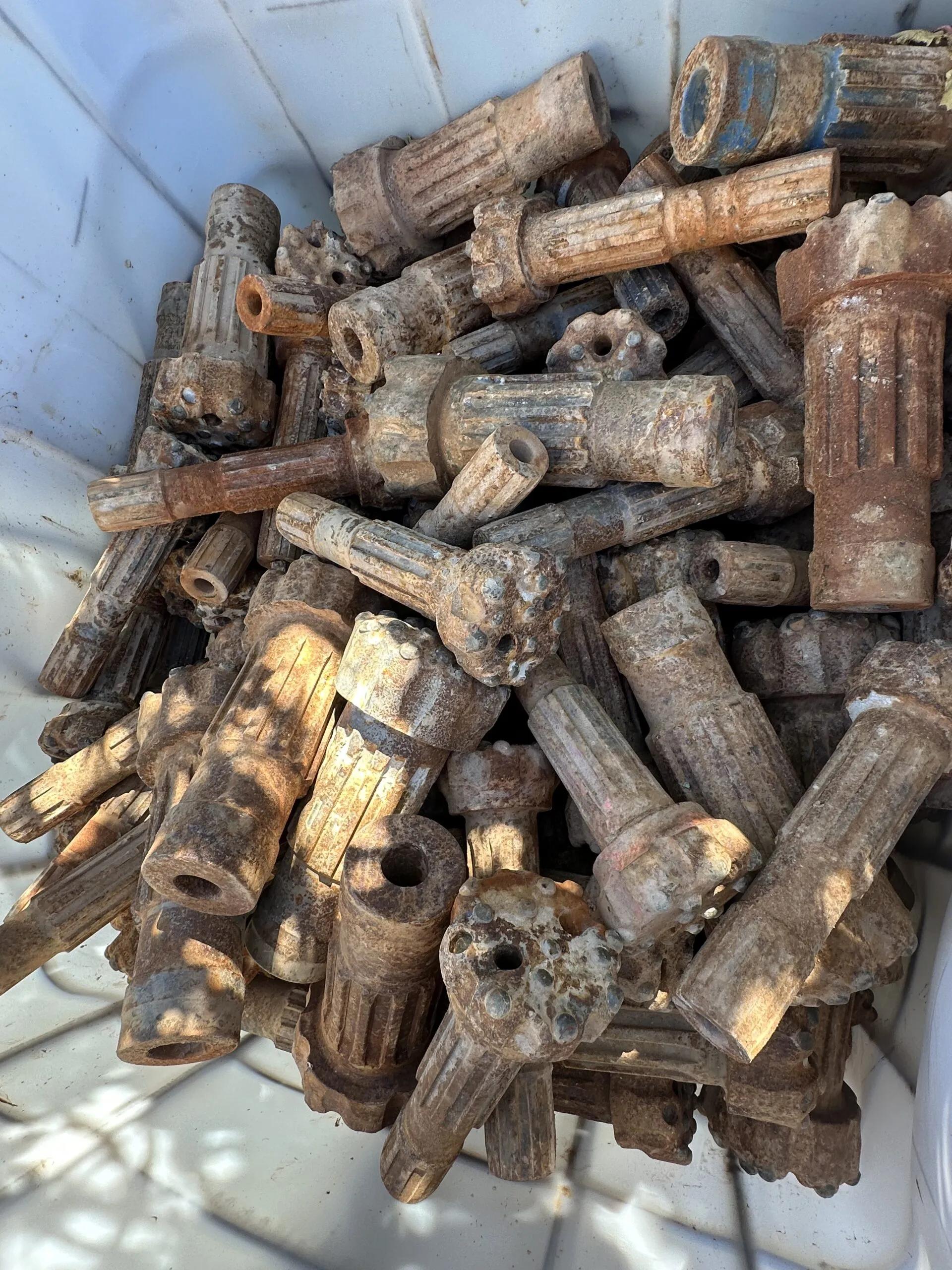 Worn DTH hammer bits and shanks in a collection tote