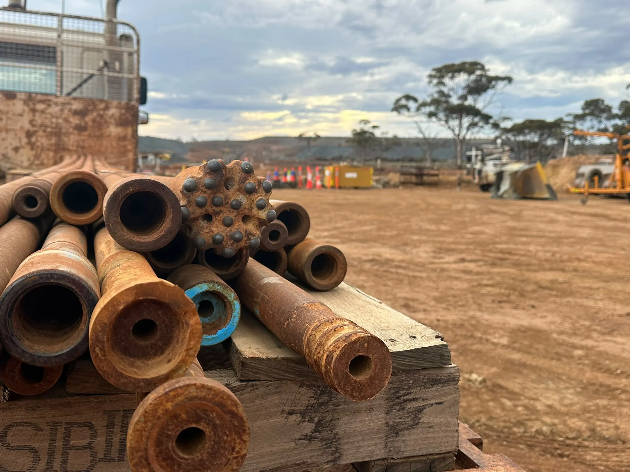 Used drill rods stacked on a pallet at a WA mine site, threaded ends and a button bit facing the camera